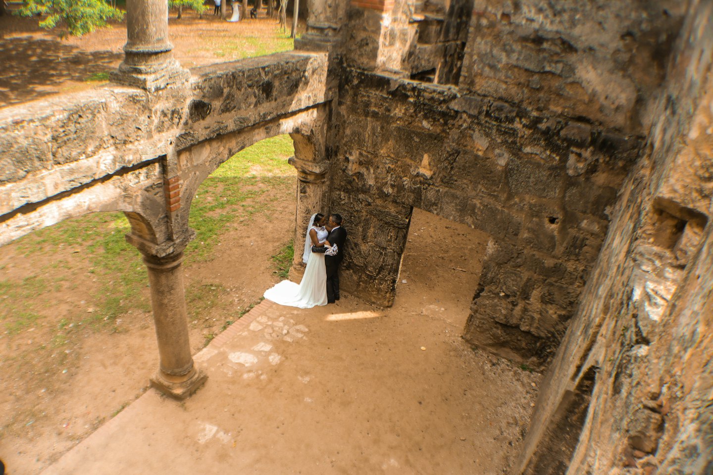 Una sposa e uno sposo si abbracciano tra le rovine di pietra consumate dal tempo.